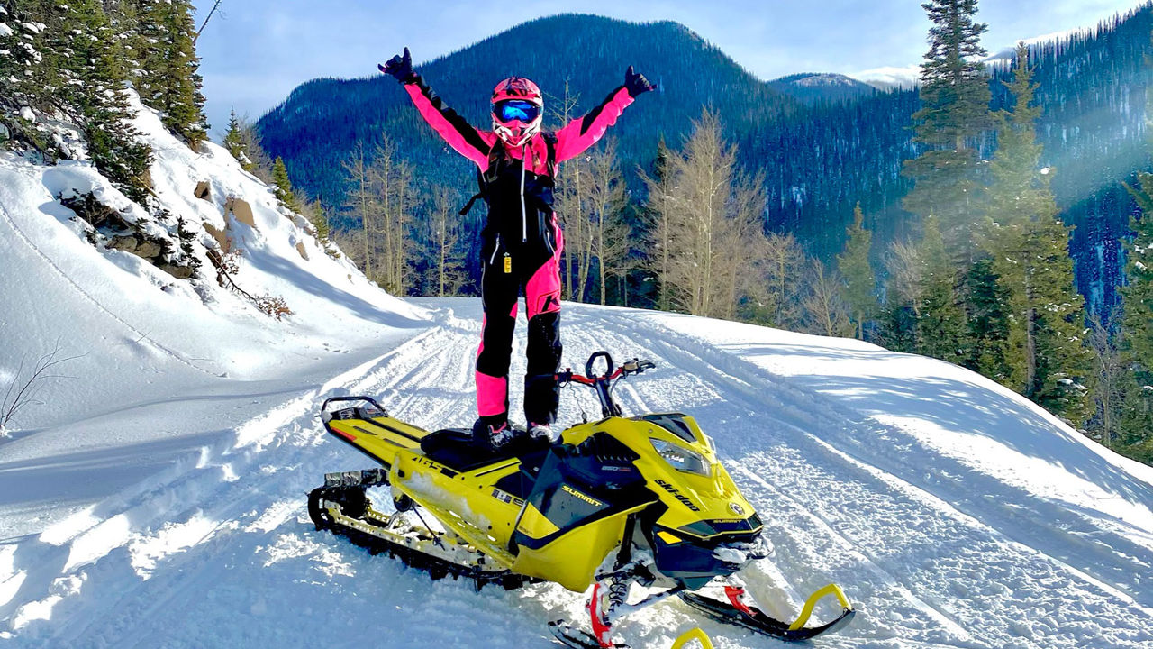 Tiffanie Hoops standing on her Ski-Doo snowmobile with a mountain landscape