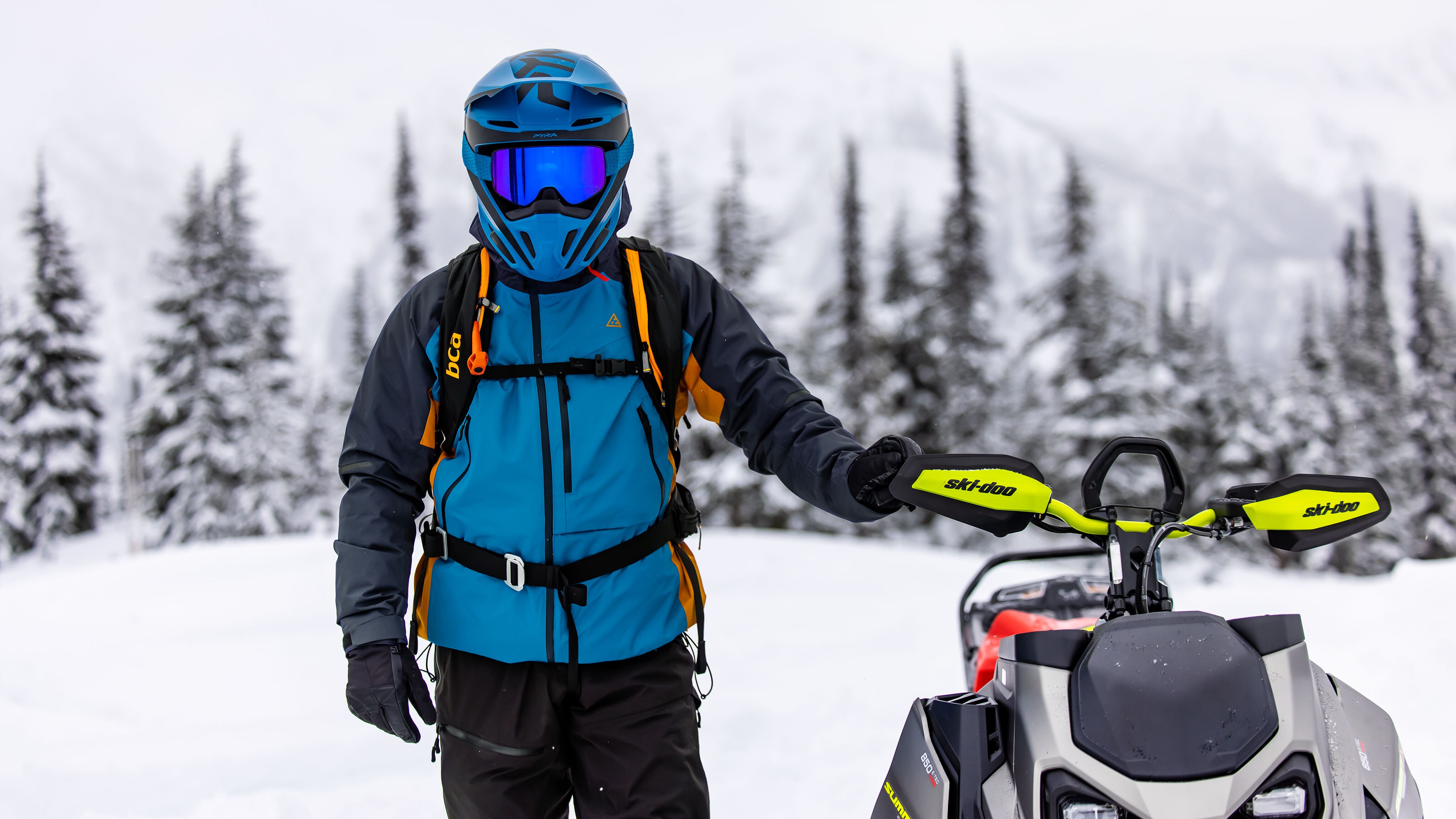 Fully geared up rider next to a 2023 Ski-Doo Summit snowmobile