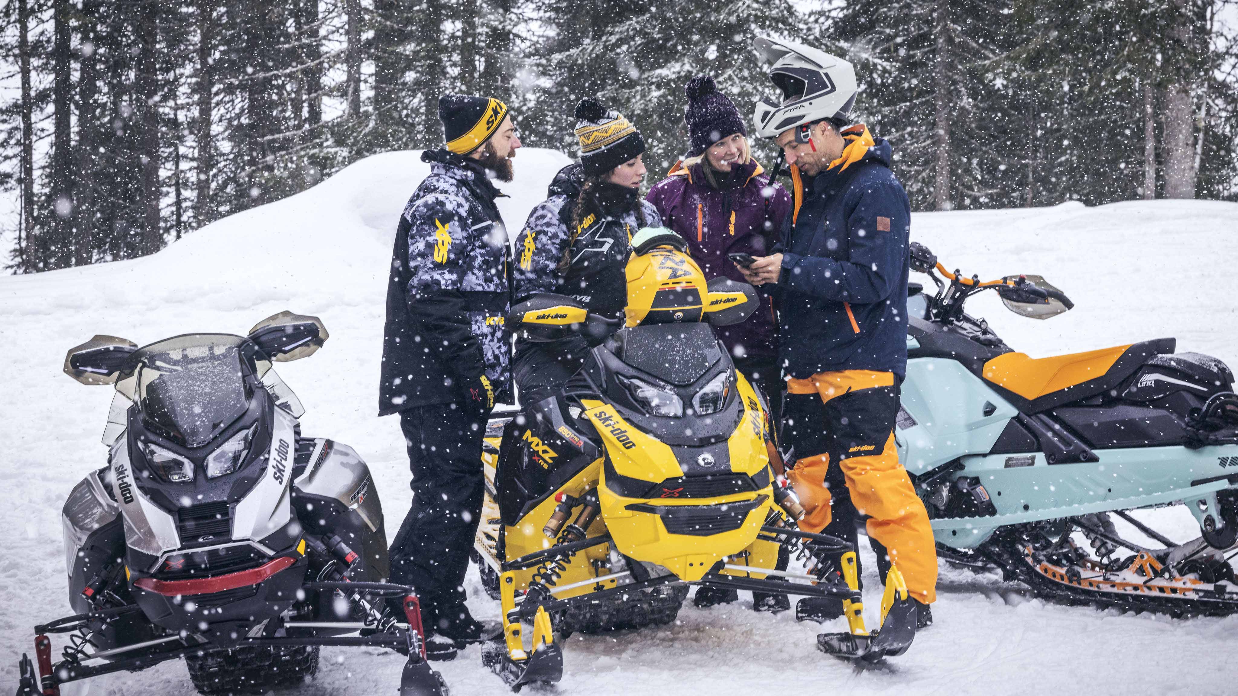 Groupe de motoneigistes regardant un cellulaire à côtes de 3 Ski-Doo