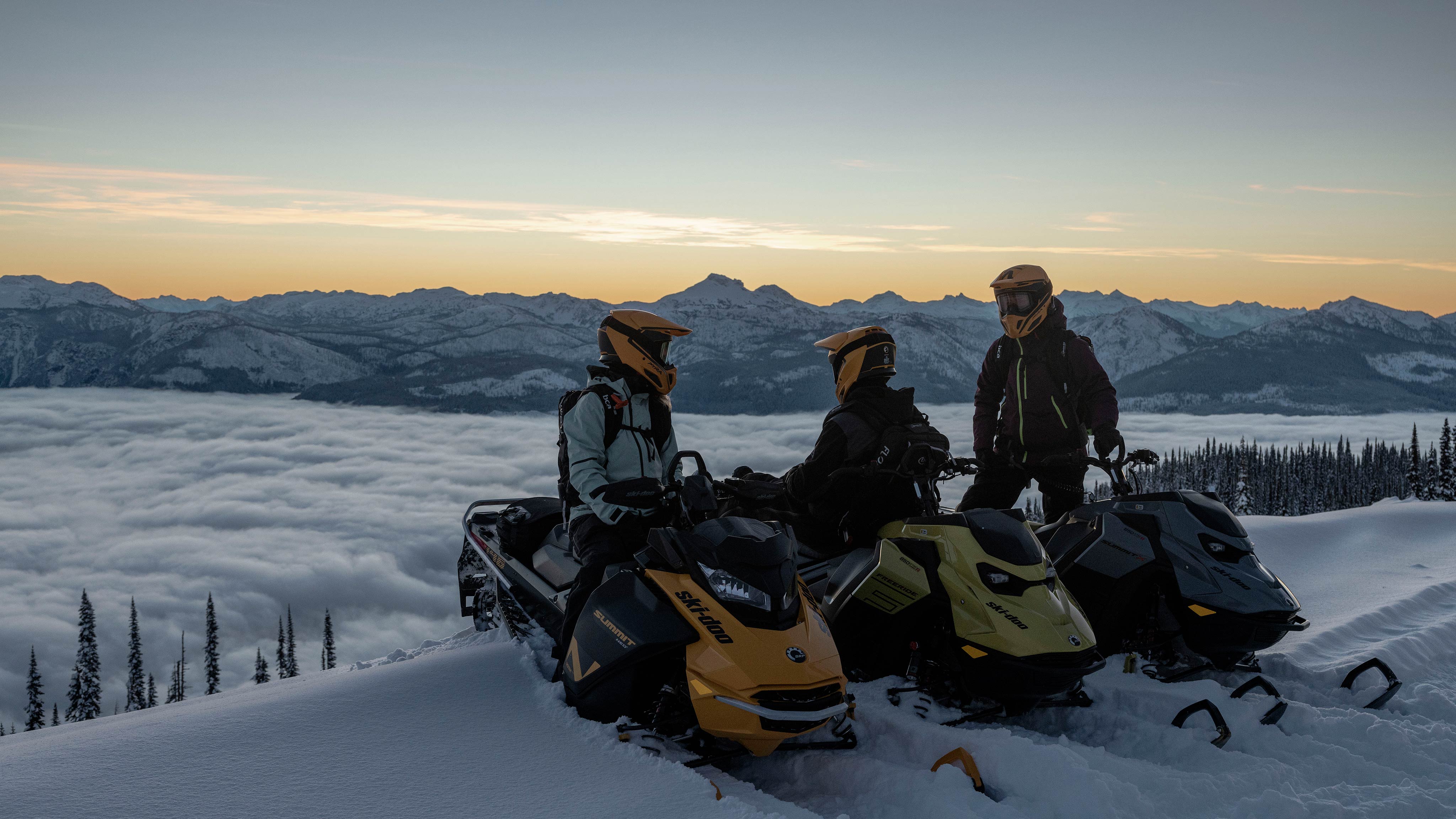 Three Ski-Doo riders on their sled at the top of a mountain