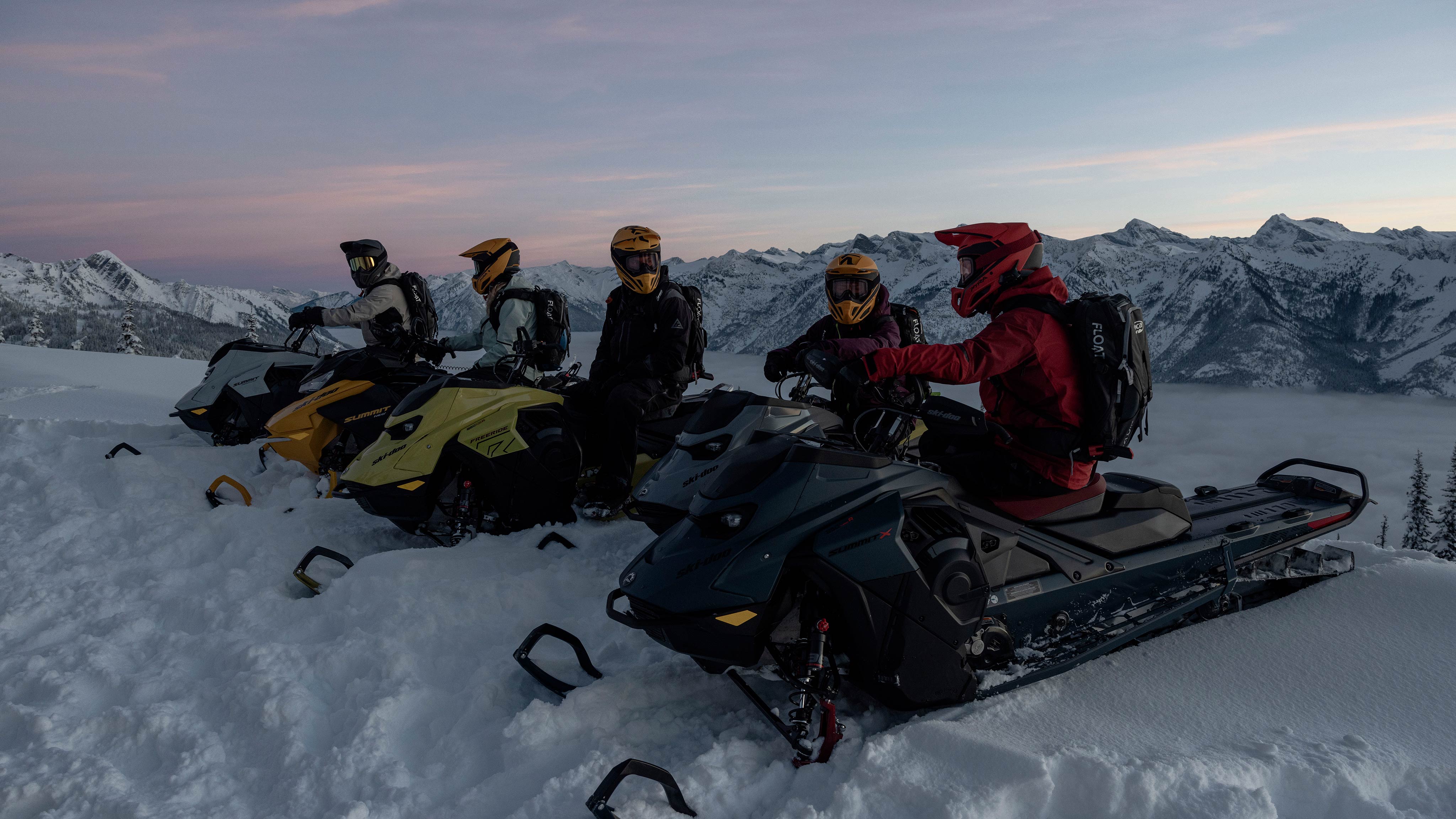 Cinq motoneigistes sur le haut d'une montagne enneigée