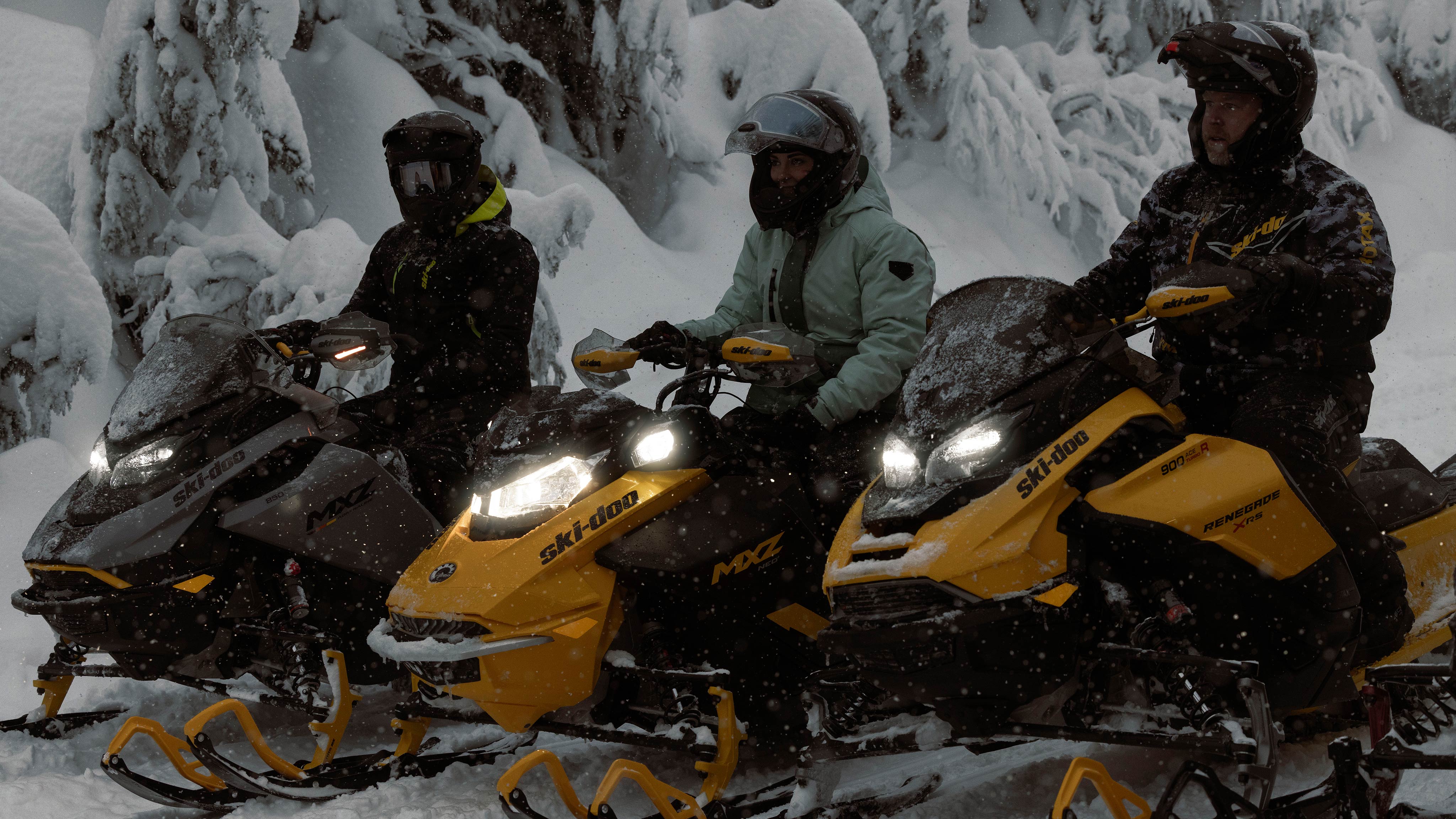 Three riders taking a break from a snowy ride on their Ski-Doo snowmobiles