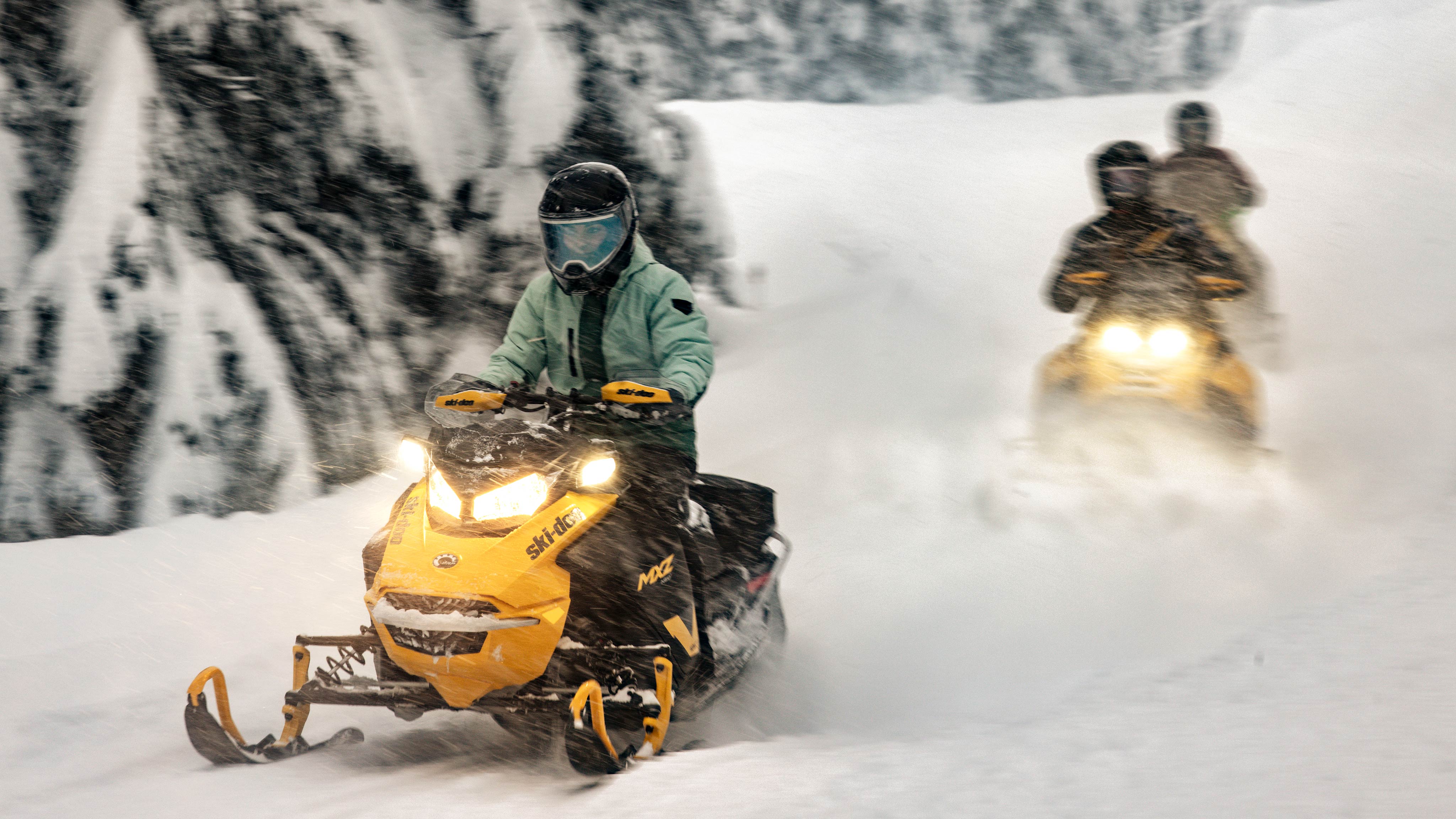 Two 2025 Ski-Doo MXZ NEO snowmobiles riding through a forest