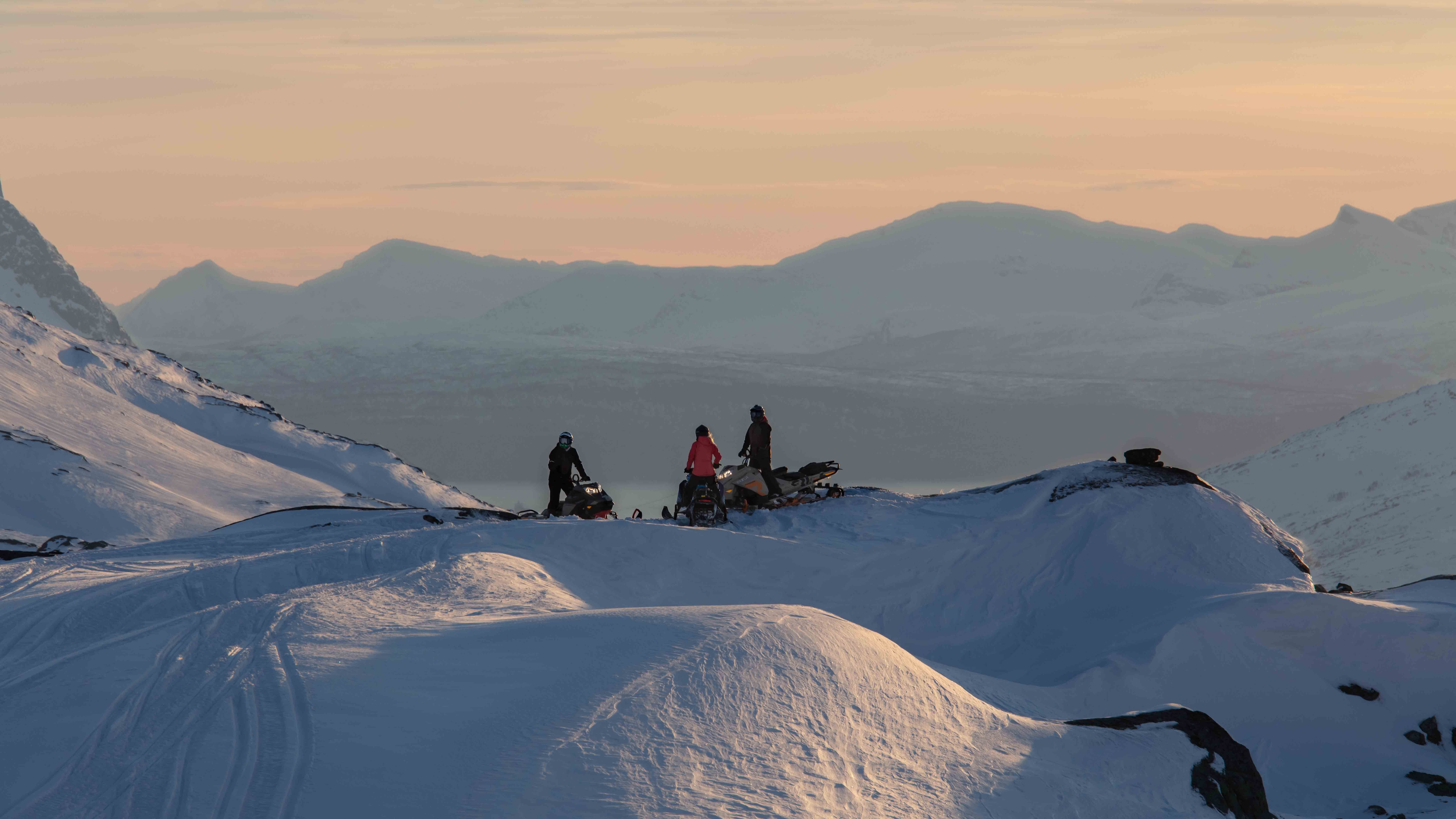 Ski-Doo-moottorikelkat pysäköitynä vuorille auringonlaskussa